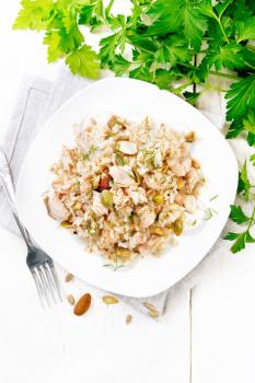 Salad of smoked salmon, rice, sunflower and pumpkin seeds, almonds, seasoned with honey and olive oil in a plate on a towel, parsley and fork on background of light wooden board on top
