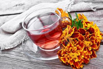 Marigold herbal tea in a glass cup and saucer, fresh flowers, burlap on the background of an old wooden board