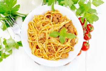 Spaghetti pasta with sauce Bolognese of minced meat, tomato juice, garlic, wine and basil in a plate, vegetable oil, spicy herb on a wooden board background from above