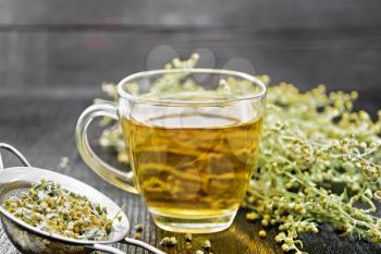 Gray wormwood herbal tea in a glass cup, fresh flowers sagebrush and metal strainer with dry wormwood flowers on dark wooden board
