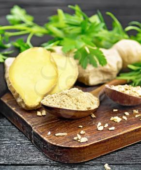 Ground ginger and flakes in two wooden spoons, ginger root, spicy herbs on a wooden board background