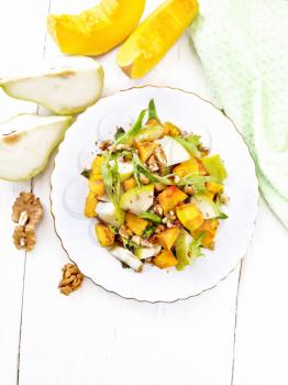 Salad of baked pumpkin, fresh pear, arugula and walnuts, seasoned with honey, balsamic vinegar, spices and vegetable oil in a plate on background of light wooden board from above