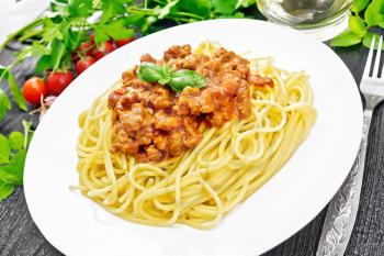 Spaghetti pasta with Bolognese sauce of minced meat, tomato juice, garlic, wine and spices in a plate, vegetable oil, spicy herb on a wooden board background