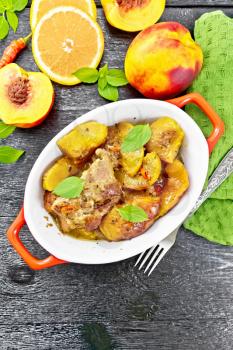 Turkey stewed with peaches, fresh hot pepper and orange sauce, basil leaves in a roasting pan, napkin, fruits on dark wooden board top