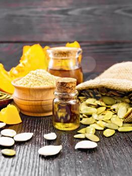 Pumpkin oil in glass vial and a jar, flour in a bowl, seeds in a spoon and bag, slices of vegetable on wooden board background