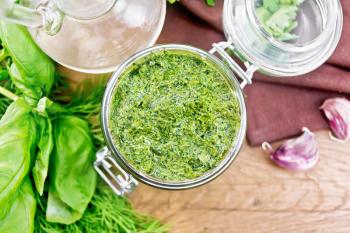 Sauce of dill, parsley, basil, cilantro, other spicy herbs, garlic and vegetable oil in a glass jar, napkin on wooden board background from above