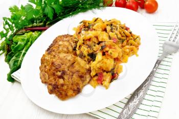 Fritters of minced meat with stewed cabbage in a plate, fork on napkin, tomatoes, parsley and chard on wooden board background