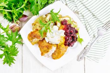 Fried turkey breast in breadcrumbs with cranberry sauce, boiled egg, baked parsnip and lettuce in a plate, napkin and fork on wooden board background from above