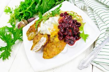 Fried turkey breast in breadcrumbs with cranberry sauce, boiled egg, baked parsnip and lettuce in a plate, napkin and fork on light wooden board background