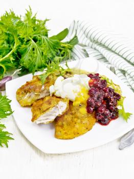 Fried turkey breast in breadcrumbs with cranberry sauce, boiled egg, baked parsnips and lettuce in a plate, towel and fork on wooden board background