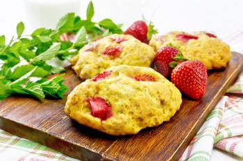 Strawberry scones with berries on a brown plank on a towel, mint sprigs on the background of light wooden board