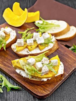 Bruschetta with baked pumpkin, salted feta cheese, ricotta, arugula and spices, napkin and vegetable slices on wooden board background