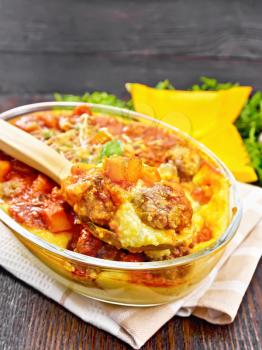 Corn porridge with meatballs, sauce of tomato, garlic and pumpkin, sprinkled with cheese, basil and spoon in a pan on towel against the background of dark wooden board