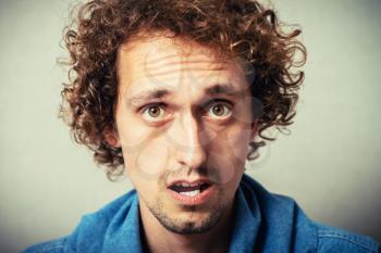 Curly young male resentment and bad mood. On a gray background