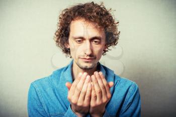 The curly-haired man looks at his hands palm gesture empty. On a gray background.
