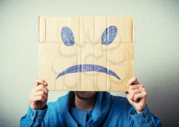 Curly man with a kraft cardboard instead of a head, a sad smiley. On a gray background.