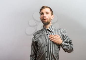 Young handsome man upset hands on heart Gesture. On a gray background
