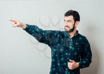 Handsome bearded Caucasian man in blue  shirt smiles and points with finger
