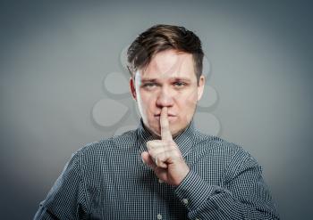 Studio portrait of a young man making a silence gesture, gray background