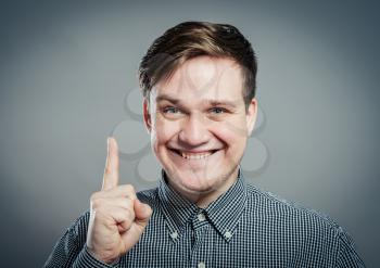 Portrait of smiling young man pointing upwards while standing against gray background. Vertical shot.