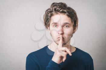 Man shows his finger to his mouth quiet. Gray background.