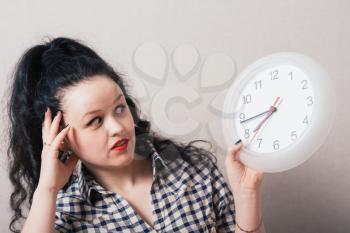 A woman looks at a wall clock with a hand on his head. On a gray background.