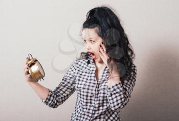 Woman looking at the alarm clock in her hand. On a gray background.