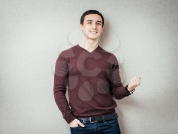young man winner gesture against a gray background 