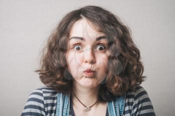portrait of a young woman with  puffing out one's cheeks  on light grey background