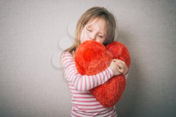 sweet little girl holds a valentines heart and thinks of love, isolated on gray background