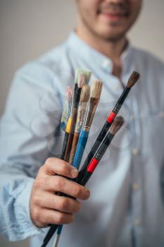 Portrait of a young male artist with brushes for painting.