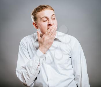 Handsome young man yawning with eyes closed, standing on grey background