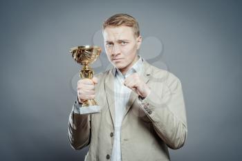 a winner with suit holding a cup/trophy showing his fist is proud over gray