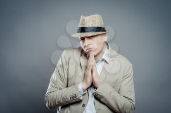 Closeup portrait desperate young man  in hat showing clasped hands, pretty please with sugar on top isolated grey wall background. Human emotion facial expression feelings, signs symbols body language