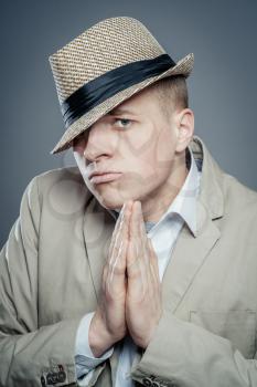 Closeup portrait desperate young man  in hat showing clasped hands, pretty please with sugar on top isolated grey wall background. Human emotion facial expression feelings, signs symbols body language