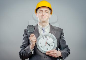 engineer man in helmet with a magnifying glass and big clock, it's time to inspection