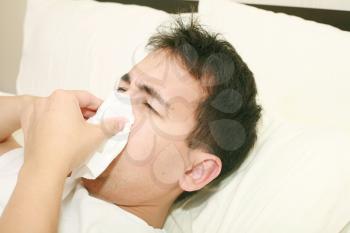 Sick man blowing his nose lying on his bed at morning 
