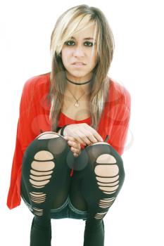 Young woman in punk attire bends over to hug her legs while looking into the camera.