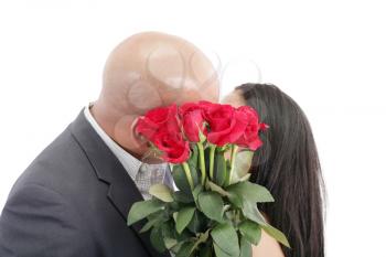 Two young dates kissing behind a bouquet of red roses