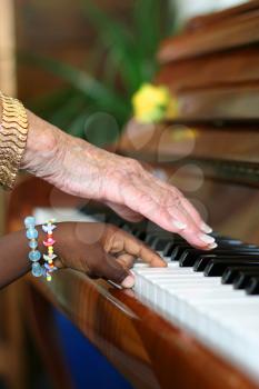 One older white hand and one younger black hand playing the piano