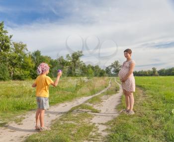 Small boy making soap bubbles with his regnant mother in the green field
