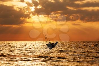 Kite surfer jumping from the water at sunset ocean

