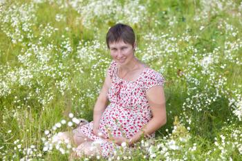 Pregnant woman sitting in chamomile background
