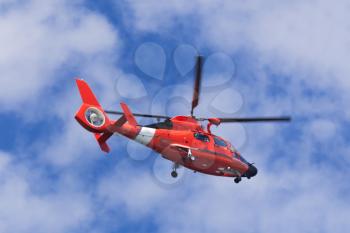 Red rescue helicopter moving in blue sky with blur propeller
