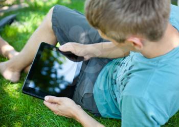 A young man uses tablet computer relaxing in green grass