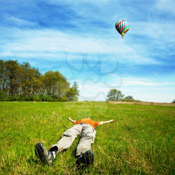 Royalty Free Photo of a Man Laying in a Field Watching a Hot Air Balloon