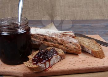 Rye baguette and jam on wooden background