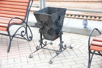 Metal decorative garbage urn near to a wooden bench