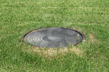 Metal manhole in a background of green grass on the field.