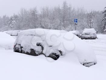 Vehicles covered with snow in the winter blizzard in the parking.